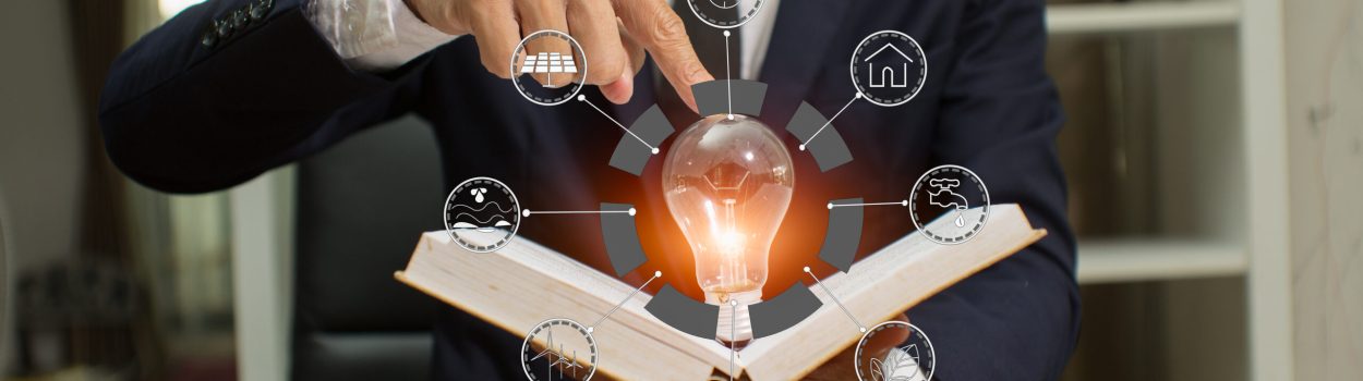 Pessoa de terno segurando um livro aberto, do qual surge uma lâmpada acesa representando uma ideia ou inovação, cercada por ícones digitais relacionados a energia, tecnologia e sustentabilidade. Imagem de capa para o blogpost: Inovação e Patente Como Proteger e Valorizar suas Ideia