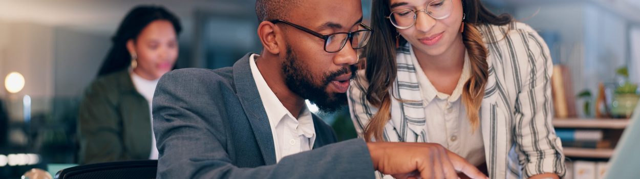 Homem e mulher em ambiente de escritório analisam juntos informações em um tablet; ele aponta para a tela enquanto ela observa atentamente, com outros colegas desfocados ao fundo, sugerindo colaboração e trabalho em equipe em um contexto profissional. Imagem de capa para o blogpost Screening de Startups.